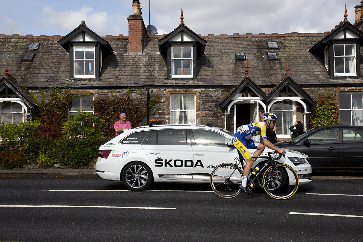 Tour of Britain 2019 - Dries van Gestle of Sport Vlaanderen Baloise passes a row of Scottish cottages with a Tour of Britain white Skoda next to him