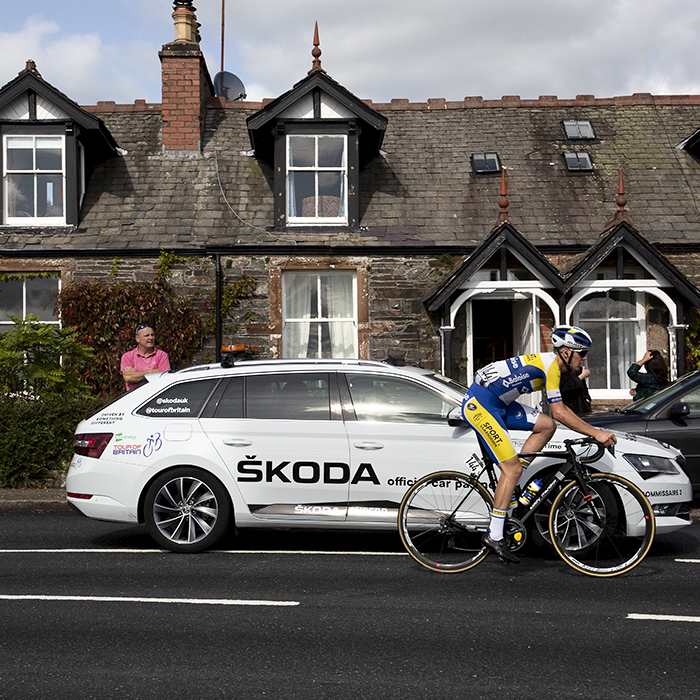 Tour of Britain 2019 - Dries van Gestle of Sport Vlaanderen Baloise passes a row of Scottish cottages with a Tour of Britain white Skoda next to him