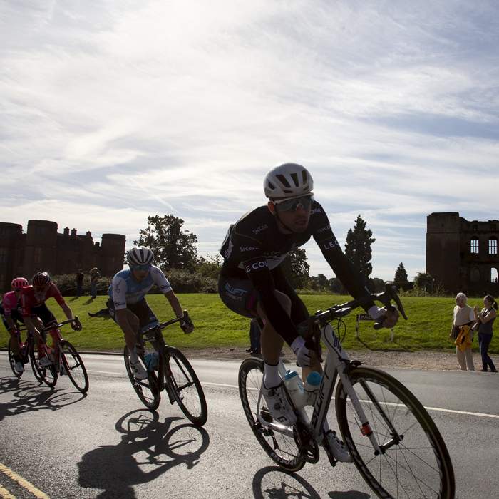 Tour of Britain 2019 - Silhouetted riders pass by Kenilworth Castle as spectators look on