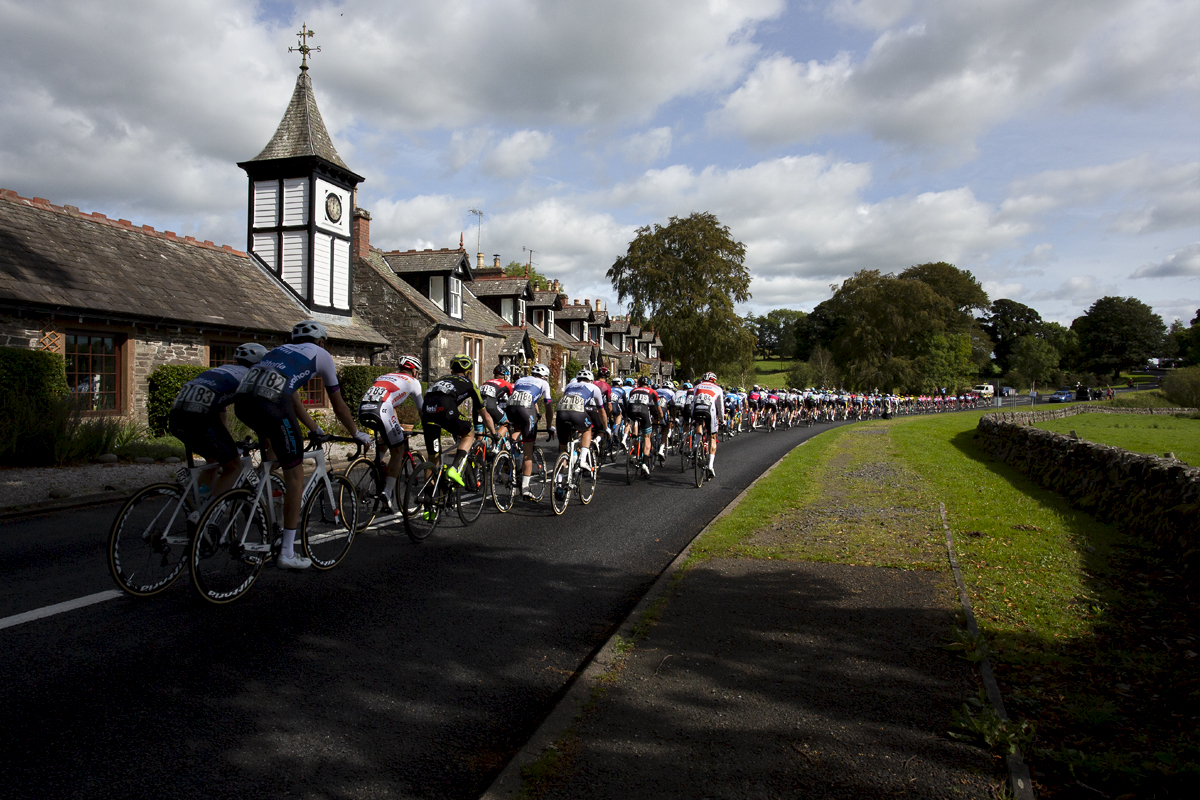 Tour of Britain 2019 - the peloton is strung out as it passes by an ornate clock tower in the village of Parton