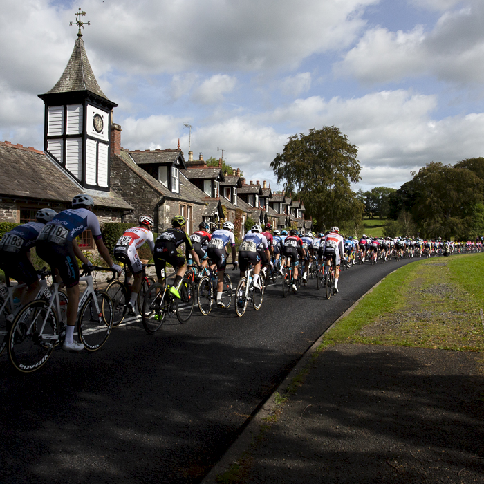 Tour of Britain 2019 - the peloton is strung out as it passes by an ornate clock tower in the village of Parton