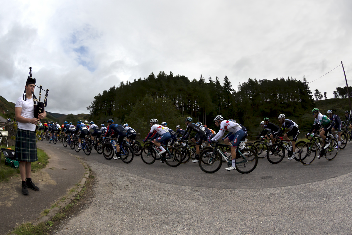 Tour of Britain 2021 - A bagpipe player serenades the peloton as it passes over Clattering Bridge in Scotland