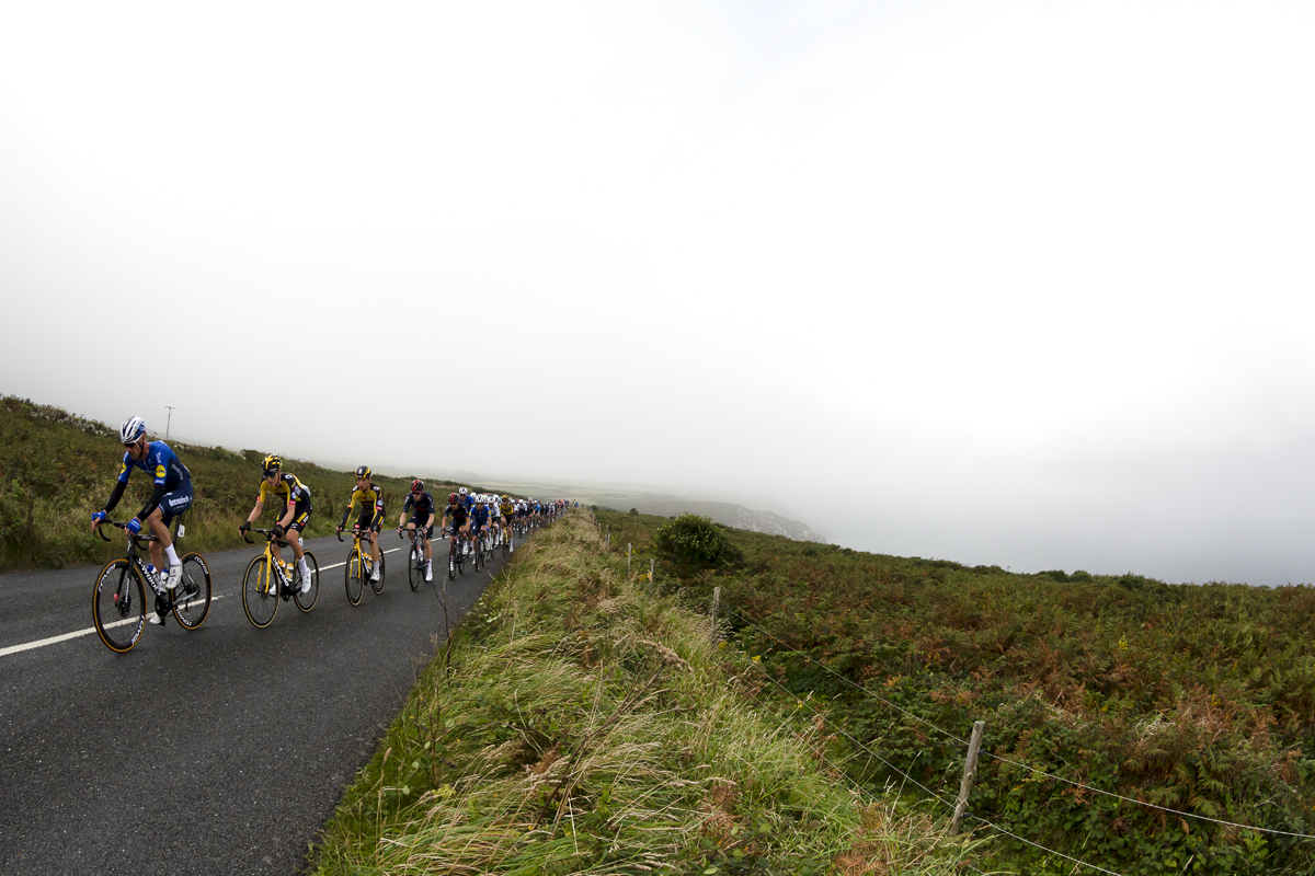 Tour of Britain 2021 - The peloton approach with the fog shrouded Trevowhan Cliff rising from the sea in the background