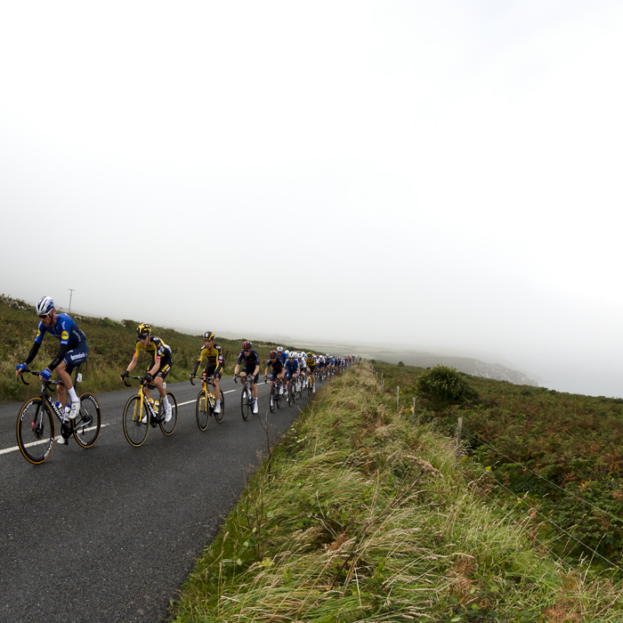 Tour of Britain 2021 - The peloton approach with the fog shrouded Trevowhan Cliff rising from the sea in the background