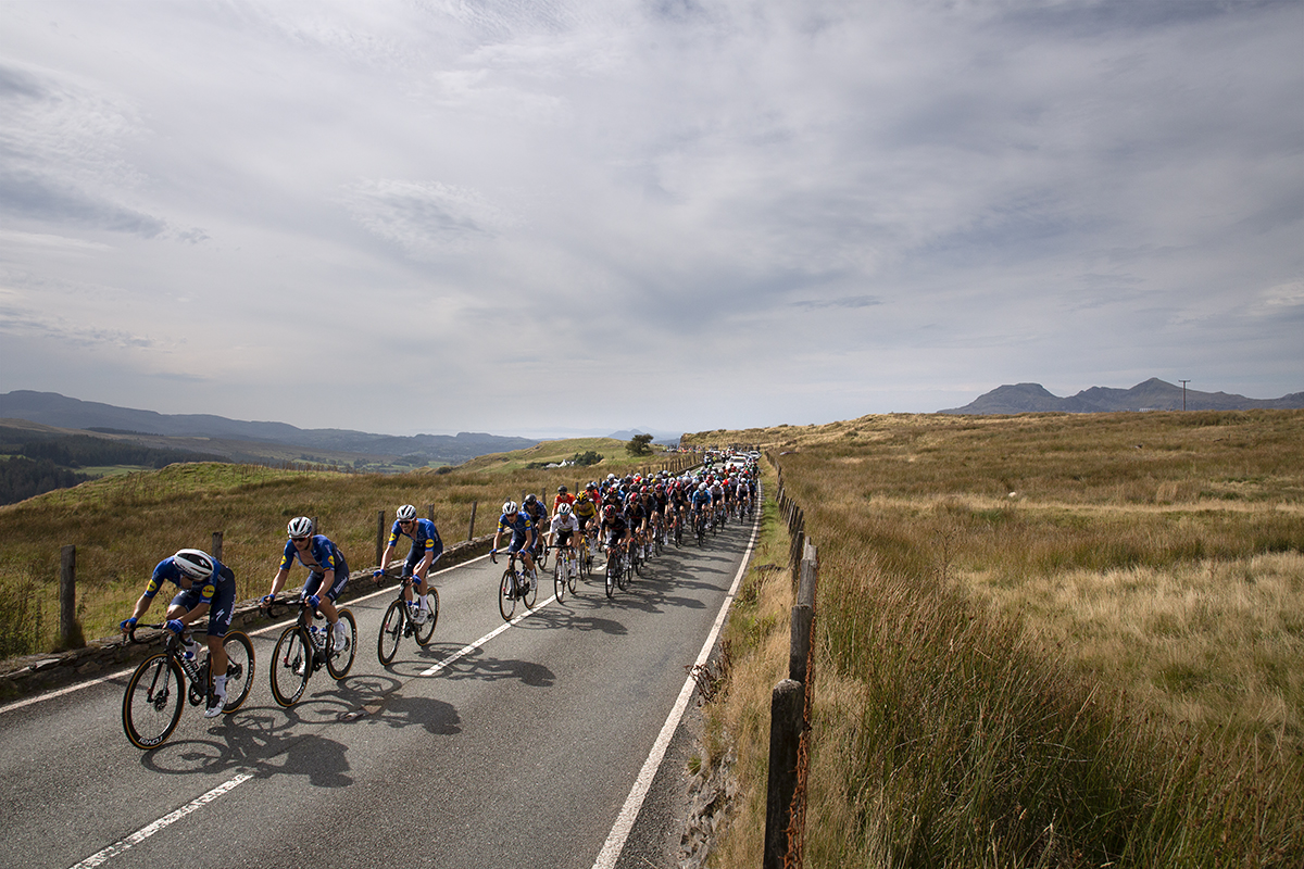 Tour of Britain 2021 - The peloton climbs Cwm Cynfal as the lead rider looks behind