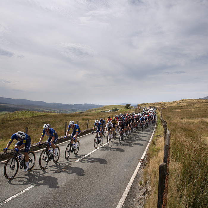 Tour of Britain 2021 - The peloton climbs Cwm Cynfal as the lead rider looks behind