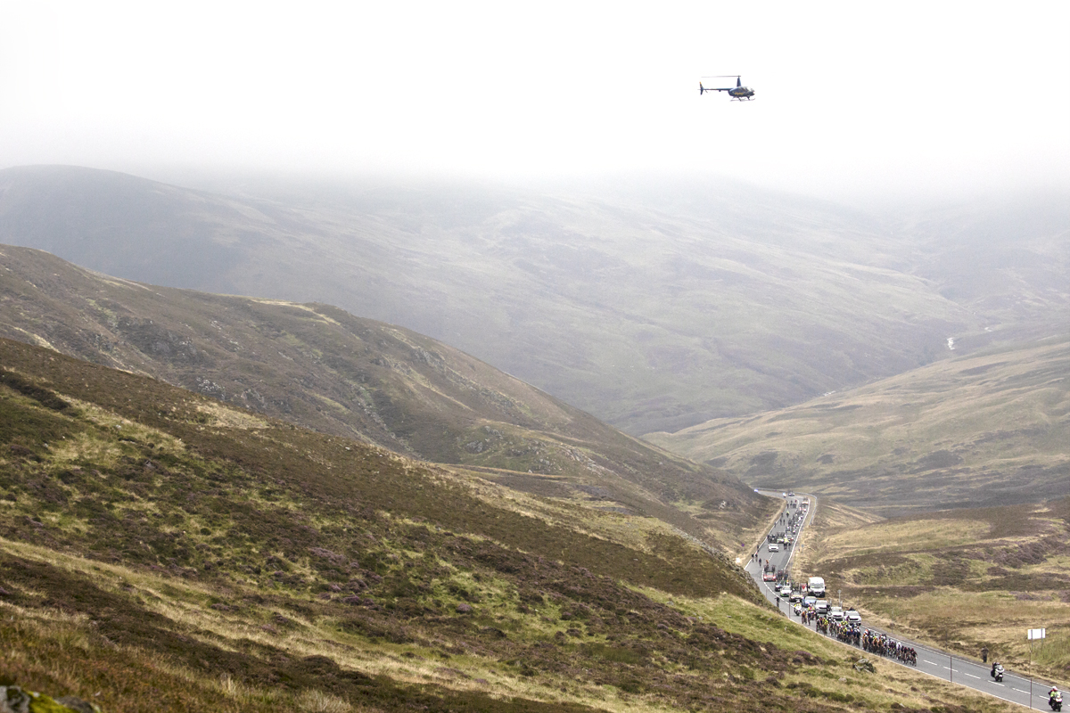 Tour of Britain 2022 -  Low cloud shrouds Cairnwell Pass as the peloton approach in the distance. 