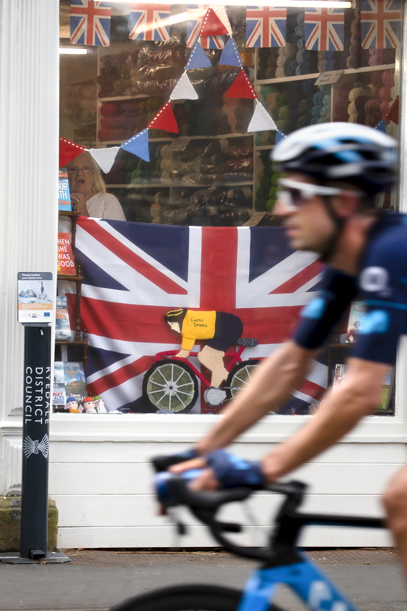 Tour of Britain 2022 - A lady in a wool shop at the side of the race gasps as she sees the riders pass