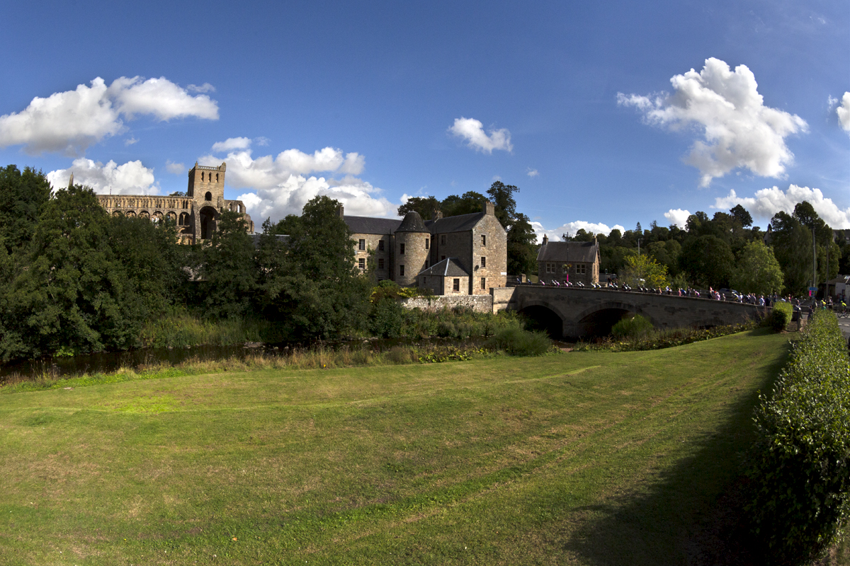 Tour of Britain 2022 - The race seen crossing a bridge on the way into Jedburgh with the Abbey in the background