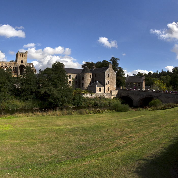 Tour of Britain 2022 - The race seen crossing a bridge on the way into Jedburgh with the Abbey in the background