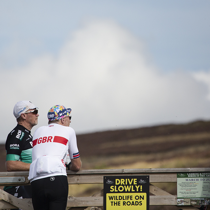 Tour of Britain 2022 - Fans dressed in cycling gear lean on gate waiting for the race to pass