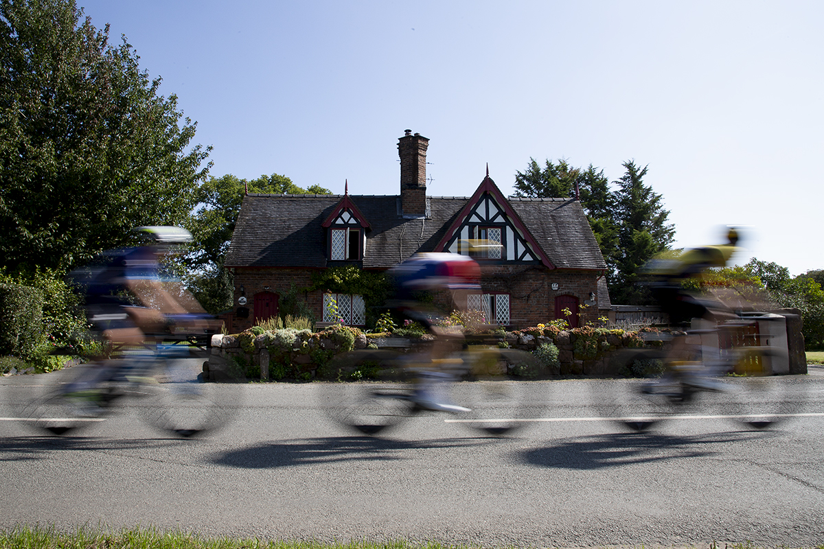 Tour of Britain 2023 - Riders speed past a cottage with a traditional cottage garden