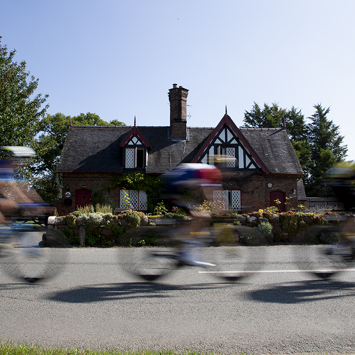 Tour of Britain 2023 - Riders speed past a cottage with a traditional cottage garden