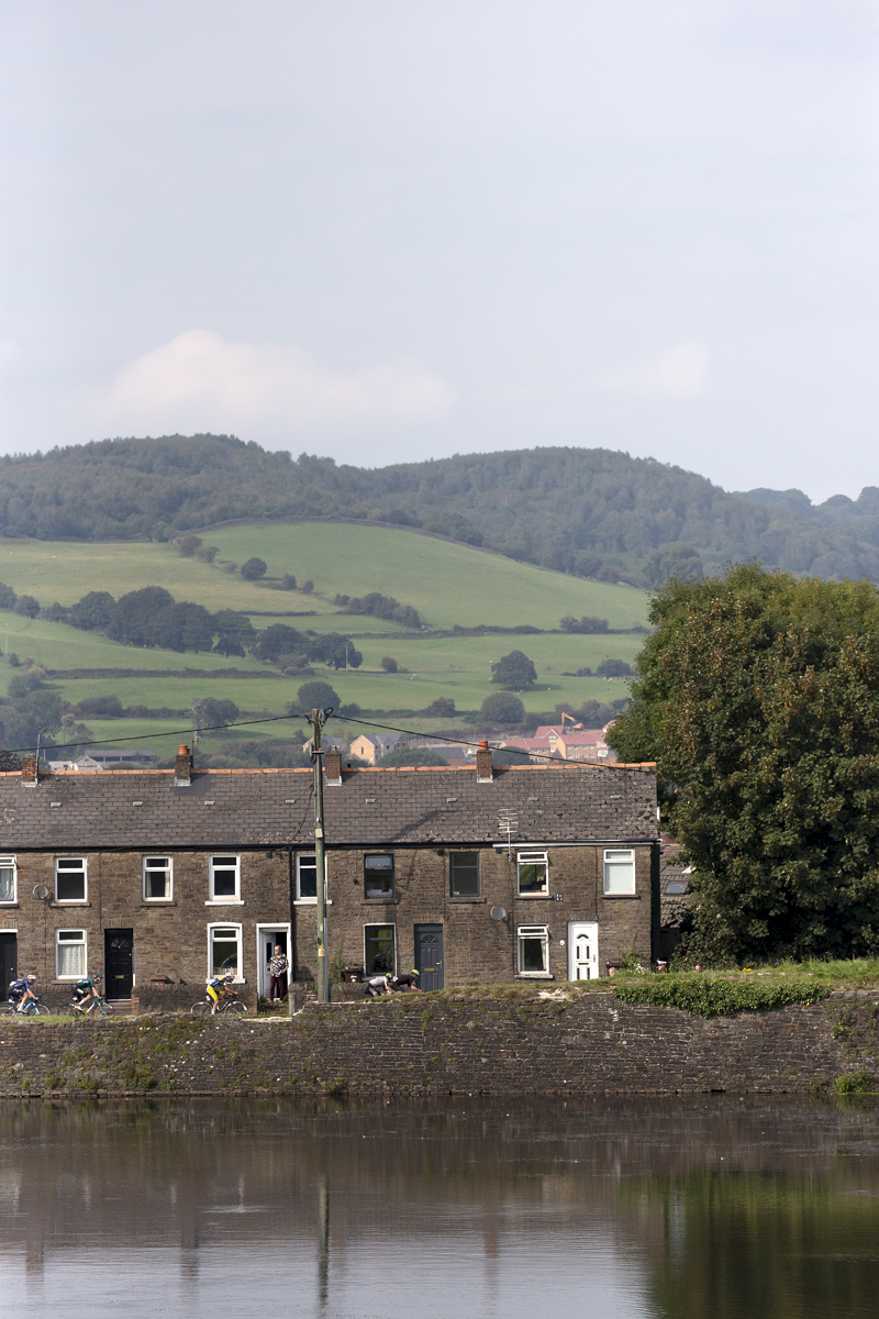 Tour of Britain 2023 - Riders pass a row of houses with the castle moat in the foreground