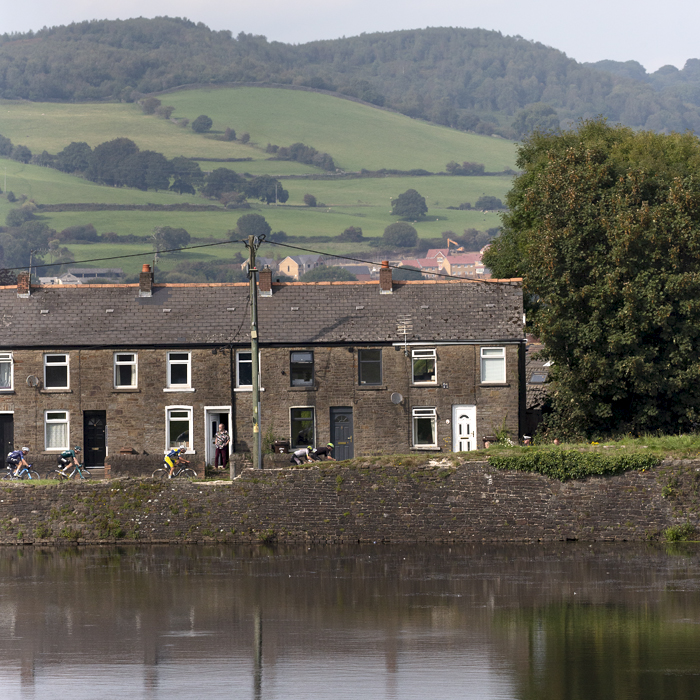 Tour of Britain 2023 - Riders pass a row of houses with the castle moat in the foreground