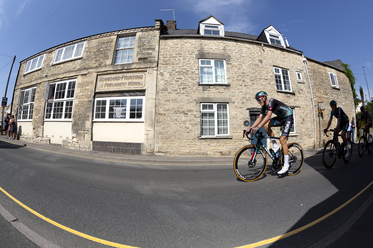 Tour of Britain 2023 - Nils Politt of BORA - hansgrohe passes sandstone buildings in the streets of Cirencester