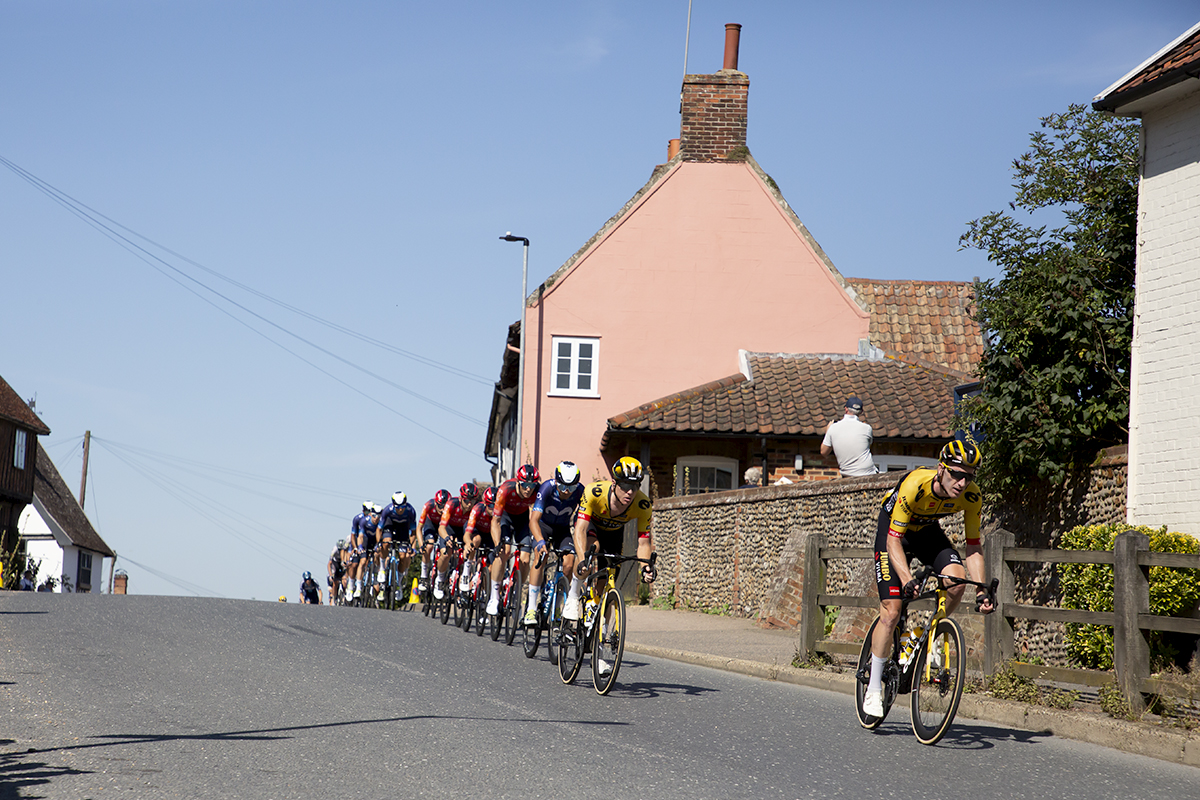 Tour of Britain 2023 - A strung out peloton passes by traditional Suffolk Pink houses in Debenham