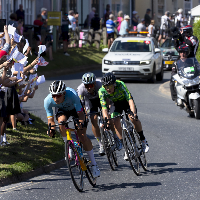 Tour of Britain 2023 - Riders race through Debenham passing a class of school children waving flags they have made