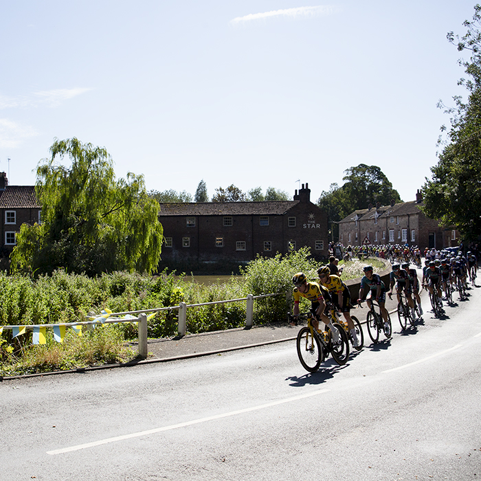 Tour of Britain 2023 - The peloton passes a village pond on its way through North Dalton