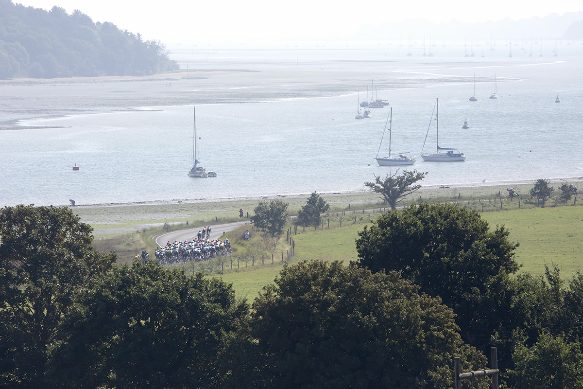 Tour of Britain 2023 - The peloton moves down the road next to the River Orwell