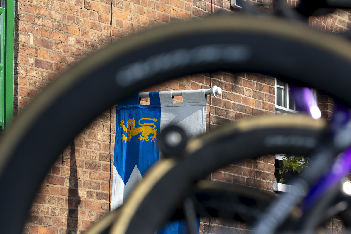 Tour of Britain 2023 - A medieval style standard shown through a bike wheel at the start in Tewkesbury