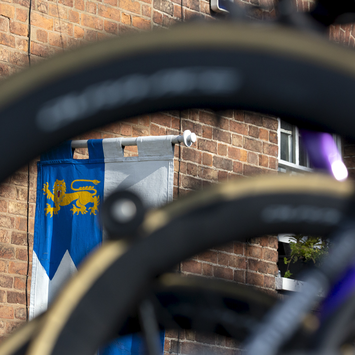 Tour of Britain 2023 - A medieval style standard shown through a bike wheel at the start in Tewkesbury