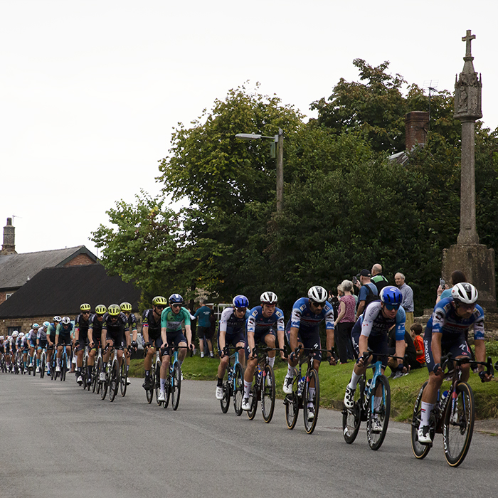 Tour of Britain 2024 - The peloton rides past the war memorial in Culworth on Stage 5