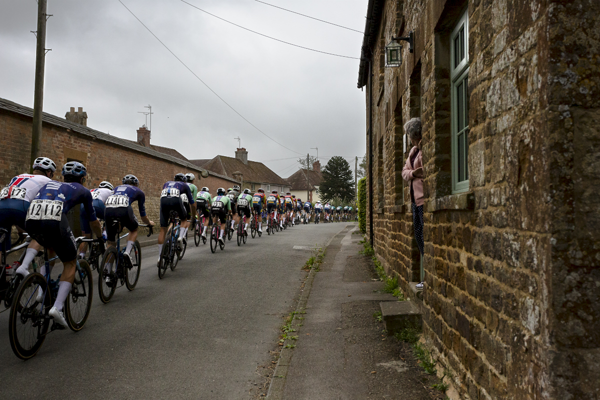 Tour of Britain 2024 - Riders pass a stone built row of cottages as a woman watches on from her doorstep