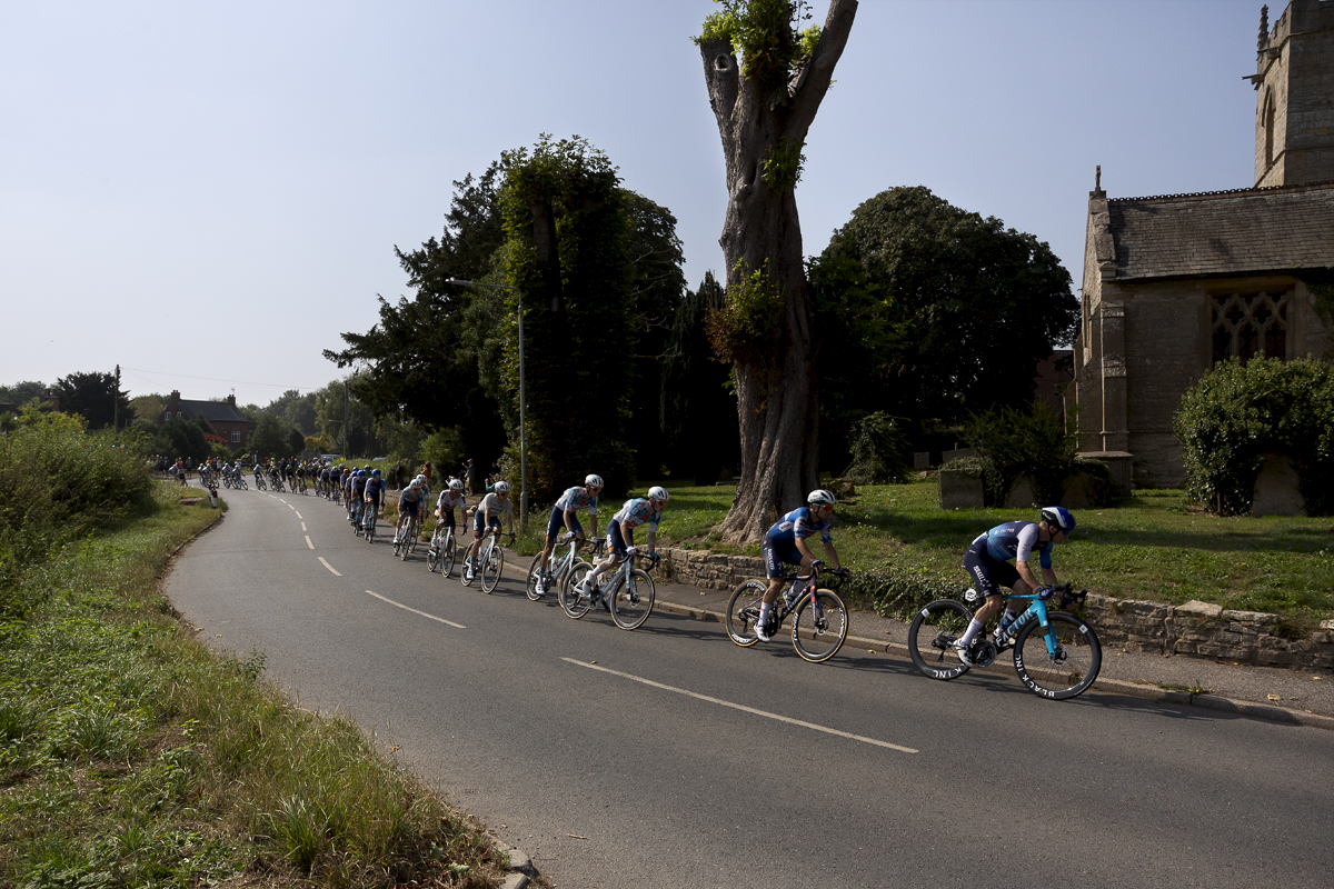 Tour of Britain 2024 - A strung out peloton passes by the church in Egmanton outside Newark on Trent