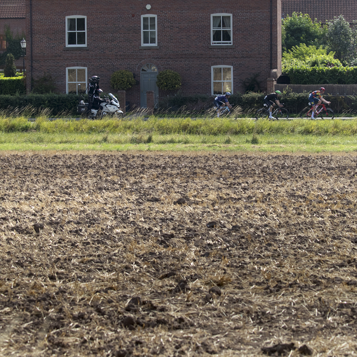 Tour of Britain 2024 - Riders seen over a ploughed field passing by a house on their way into Egmanton