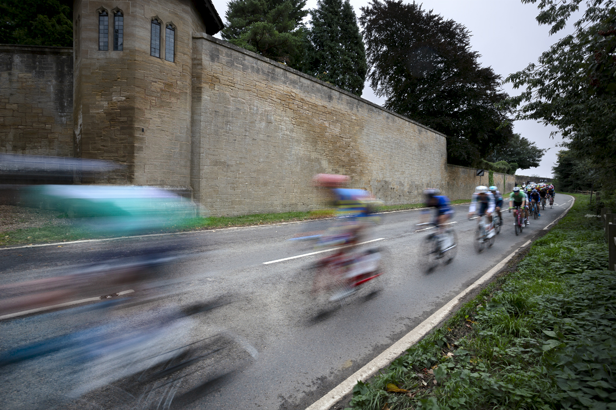 Tour of Britain 2024 - The peloton speed past the austere walls of Hooton Pagnell Hall on their way into the village