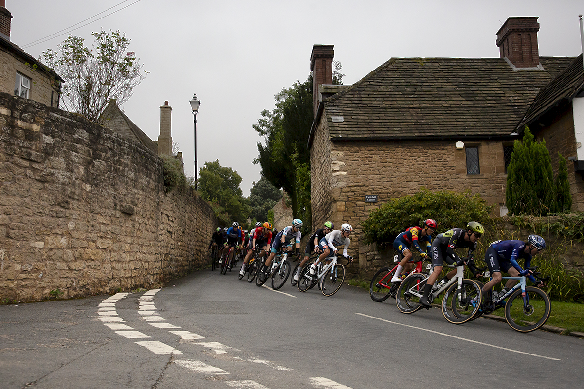 Tour of Britain 2024 - Riders pass through a corridor of honey coloured stone buildings on the way through Hooton Pagnell near Doncaster