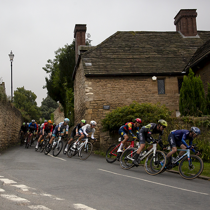 Tour of Britain 2024 - Riders pass through a corridor of honey coloured stone buildings on the way through Hooton Pagnell near Doncaster