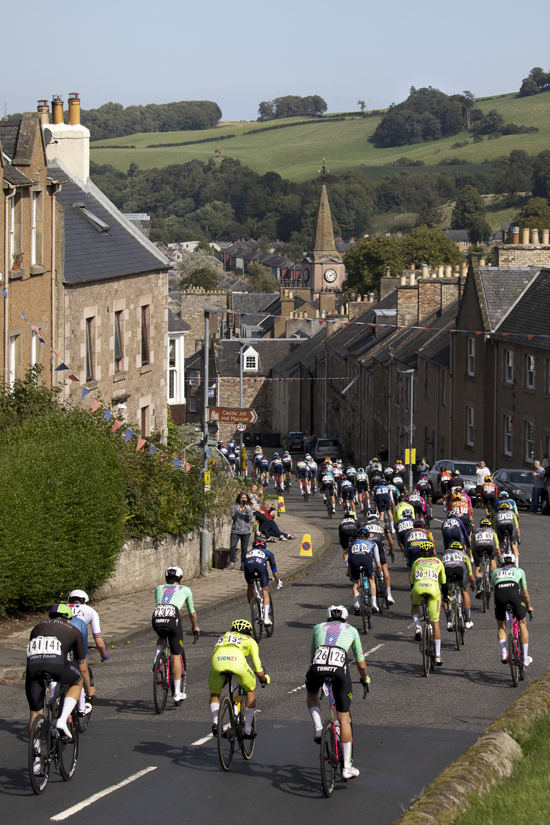 Tour of Britain 2024 - The race passes through a street lined with stone buildings in the border town of Jedburgh