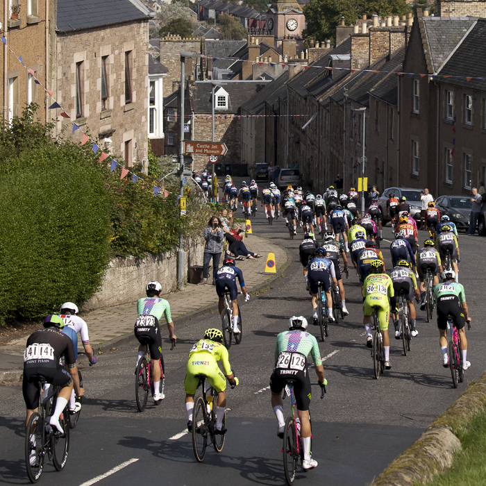 Tour of Britain 2024 - The race passes through a street lined with stone buildings in the border town of Jedburgh