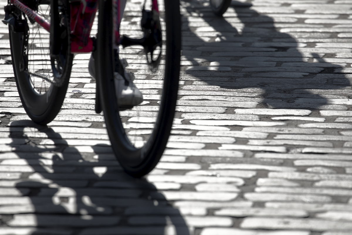 Tour of Britain 2024 - Shadows of the riders cast by the strong late summer sun in the grey cobbles of Kelso