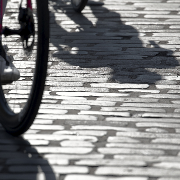 Tour of Britain 2024 - Shadows of the riders cast by the strong late summer sun in the grey cobbles of Kelso