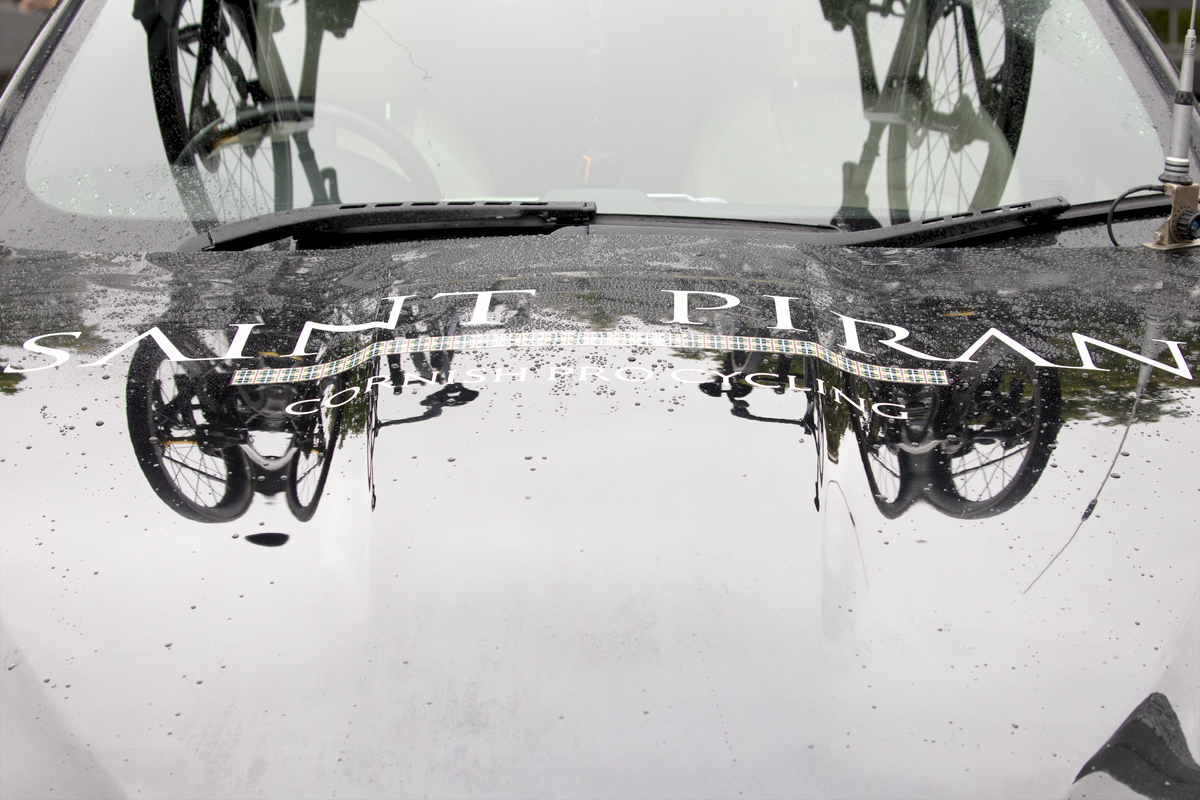 Tour of Britain 2024 - Bikes reflected on the rain spattered bonnet of the Saint Piran team car