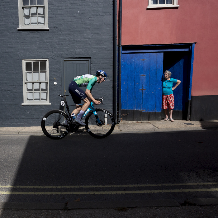 Tour of Britain 2024 - Stevie Williams and Ethan Vernon of Israel - Premier Tech pass by cottages while a women views them from her doorway