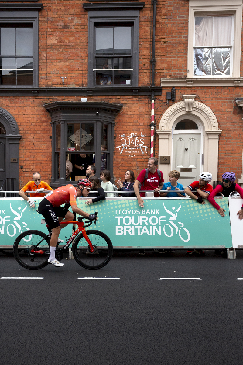 Tour of Britain 2024 - Tobias Foss passes by fans banging the advertising hoardings while others look on from inside a barbers