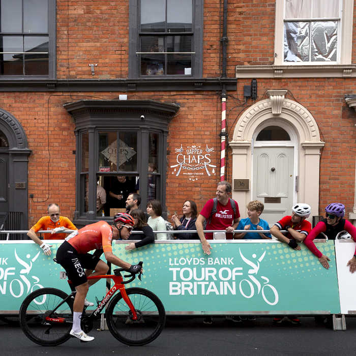 Tour of Britain 2024 - Tobias Foss passes by fans banging the advertising hoardings while others look on from inside a barbers