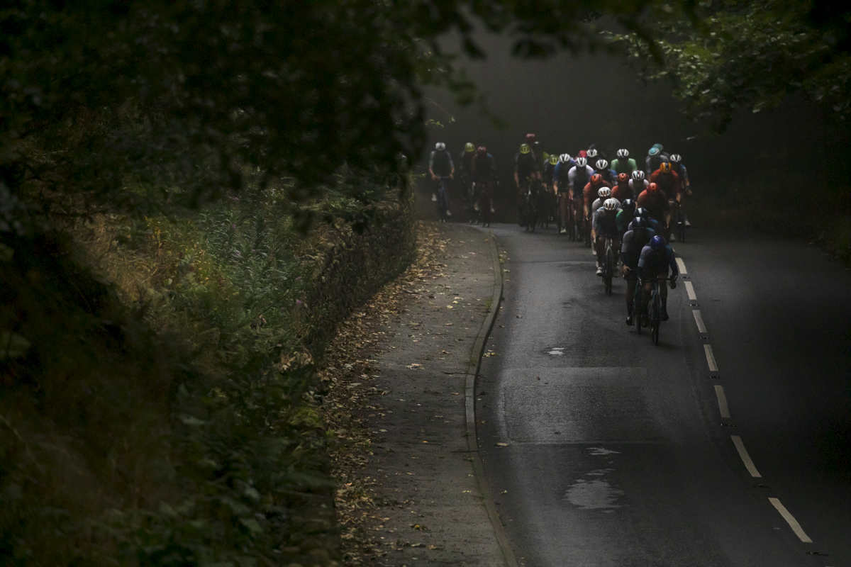 Tour of Britain 2024 - The peloton descend through the gloom with the trees beginning to shed their leaves near Wentworth Castle