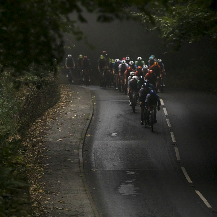 Tour of Britain 2024 - The peloton descend through the gloom with the trees beginning to shed their leaves near Wentworth Castle