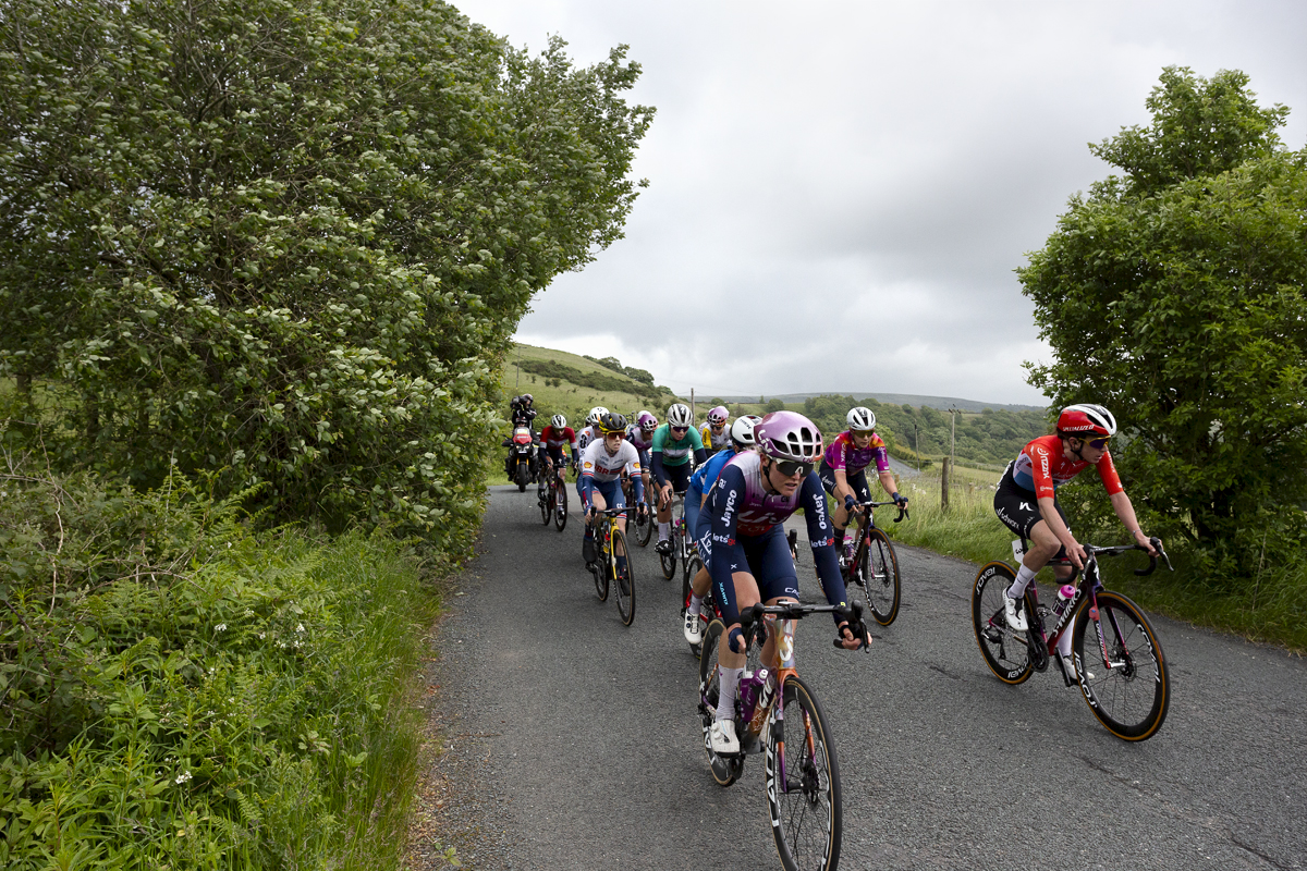 Tour of Britain Women’s 2024 - The peloton on a narrow country road with moorland in the background