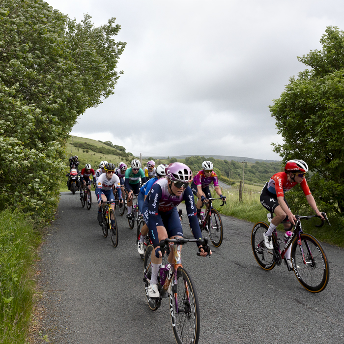 Tour of Britain Women’s 2024 - The peloton on a narrow country road with moorland in the background