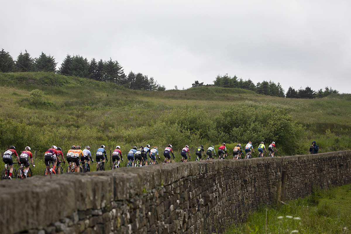 Tour of Britain Women’s 2024 - Rear view of the peloton as they make their way past a stone wall on Grains Bar