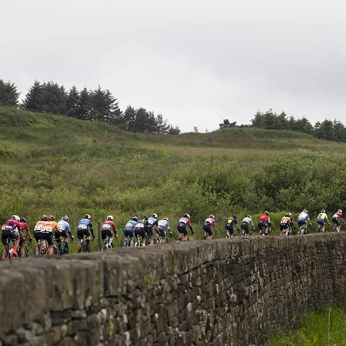 Tour of Britain Women’s 2024 - Rear view of the peloton as they make their way past a stone wall on Grains Bar