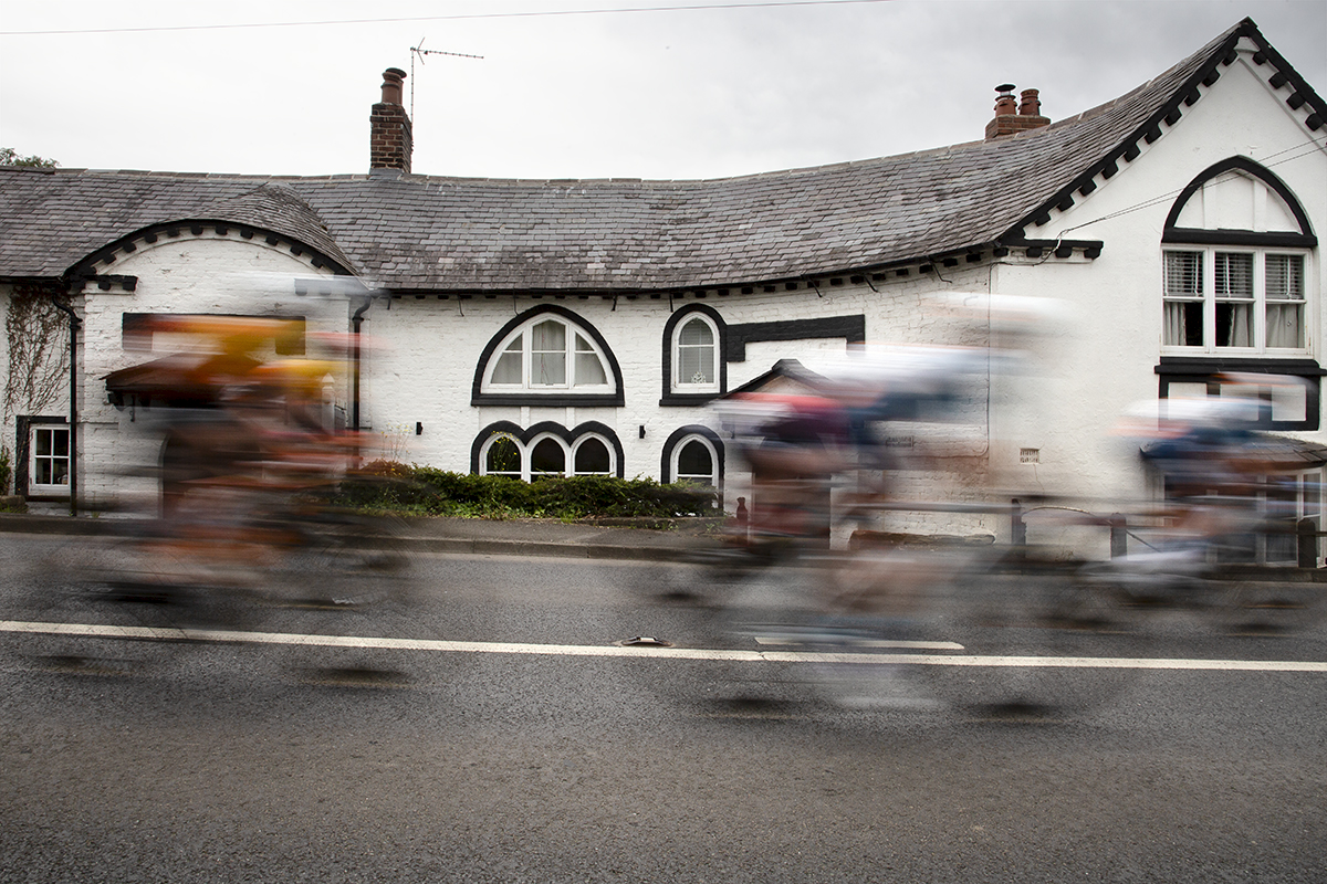 Tour of Britain Women’s 2024 - Riders speed past a white house in Marford