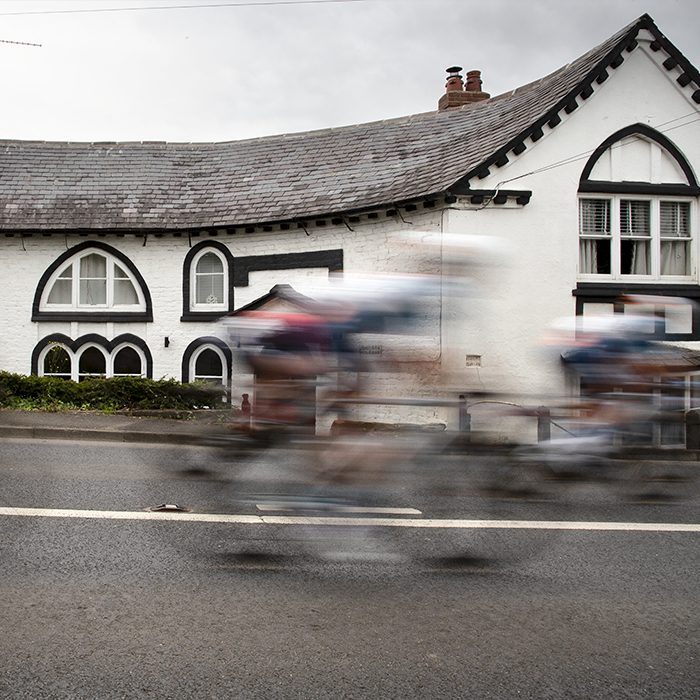 Tour of Britain Women’s 2024 - Riders speed past a white house in Marford