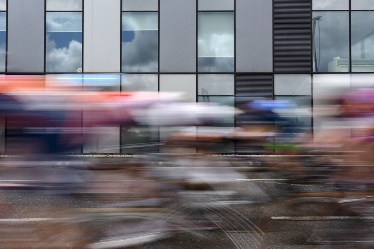 Tour of Britain Women’s 2024 - Riders speed past a modern office block in Warrington